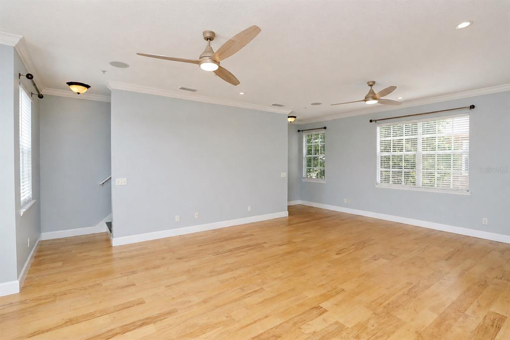 An empty room with light blue walls, hardwood floors, and two ceiling fans — 2611 ESPANA COURT, TAMPA, FL