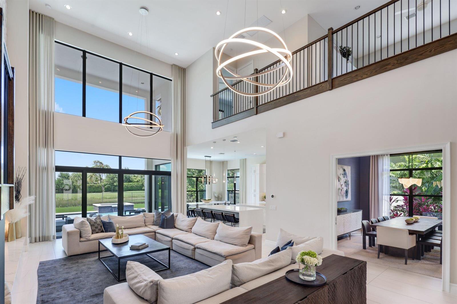 A spacious living room with high ceilings, large windows, modern chandeliers, and an open floor plan — 9275 Biaggio Road, Boca Raton FL 33496, BOCA RATON, FL