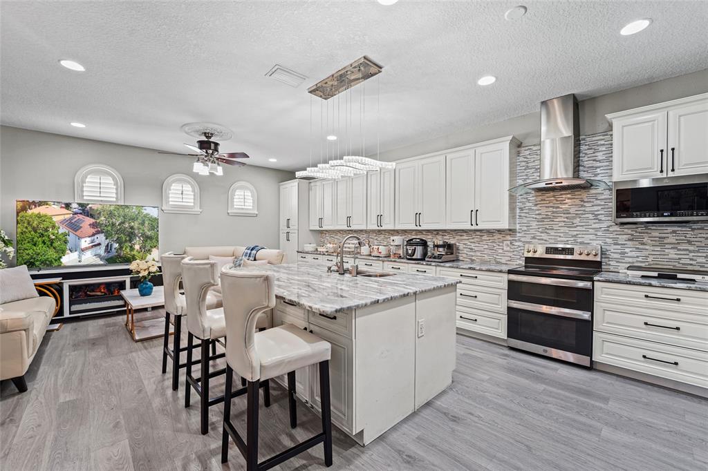 A kitchen features white cabinetry, a marble-topped island, stainless steel appliances, and gray flooring — 4202 N HOWARD AVENUE, TAMPA, FL