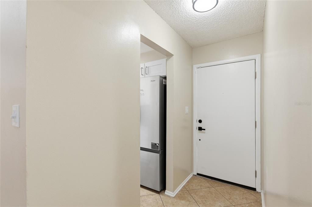 A view of an entryway with tiled floors, a white door, and a nearby refrigerator — 108 WESTWIND COURT, SANFORD, FL