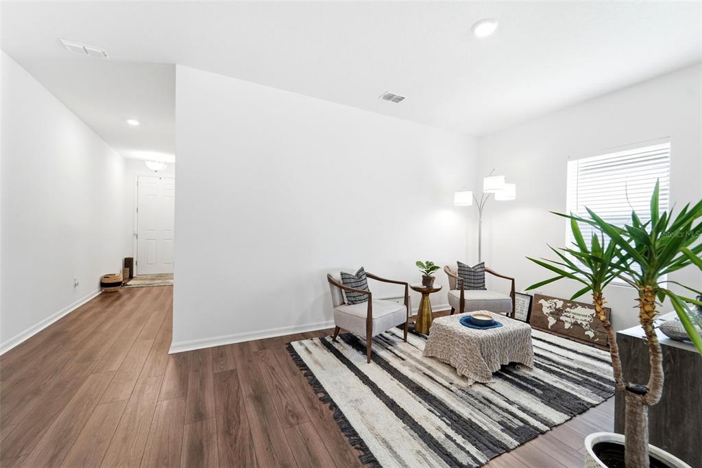 A living room features wood-look flooring, a striped area rug, two armchairs, and a floor lamp — 1525 PLAYWRIGHT DRIVE, DELAND, FL