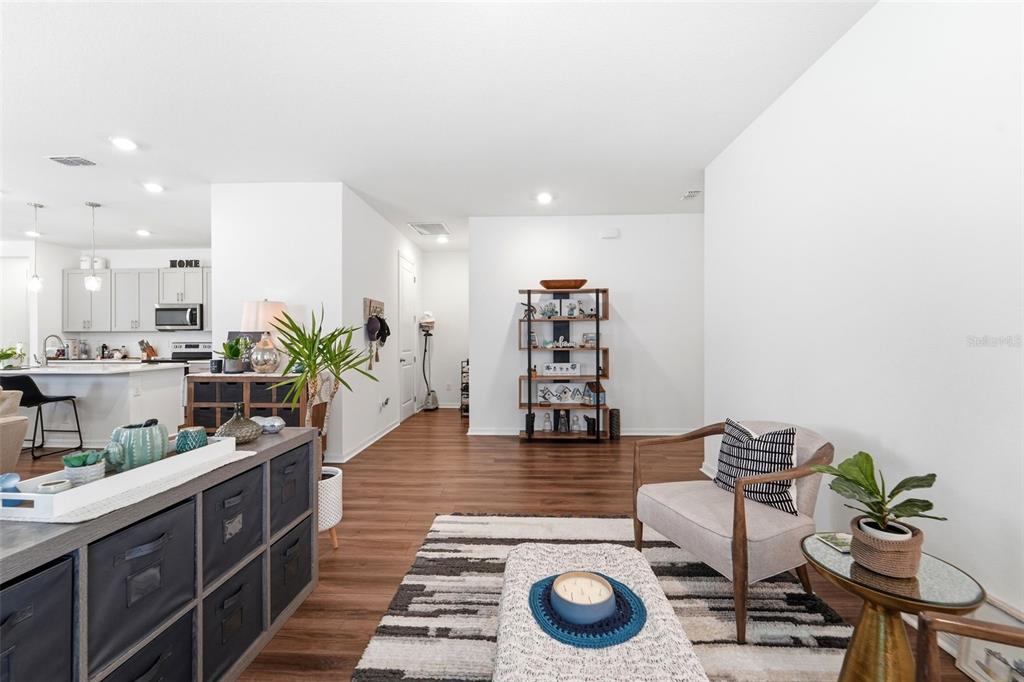 A living room with wood-look flooring, a patterned rug, a bookshelf, and an open kitchen — 1525 PLAYWRIGHT DRIVE, DELAND, FL
