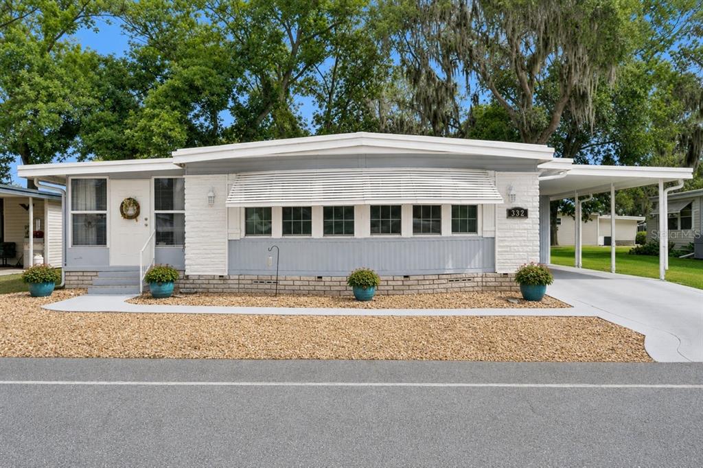A single-story manufactured home with a white brick facade, gray siding, and an attached carport — 332 HAWTHORNE BOULEVARD, LEESBURG, FL