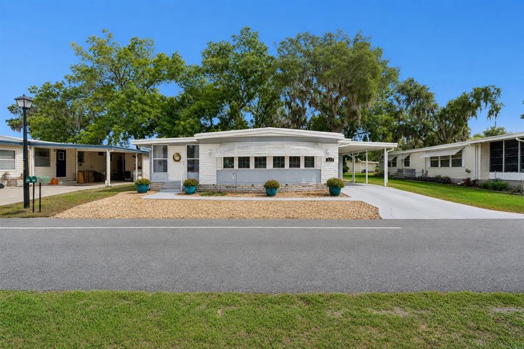 A single-story manufactured home with a white facade, a carport, and a gravel front yard — 332 HAWTHORNE BOULEVARD, LEESBURG, FL