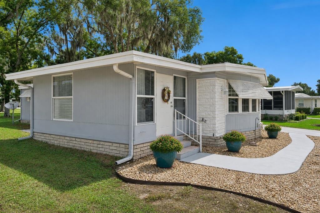 A single-story manufactured home with gray siding, a white brick accent, and a gravel yard — 332 HAWTHORNE BOULEVARD, LEESBURG, FL