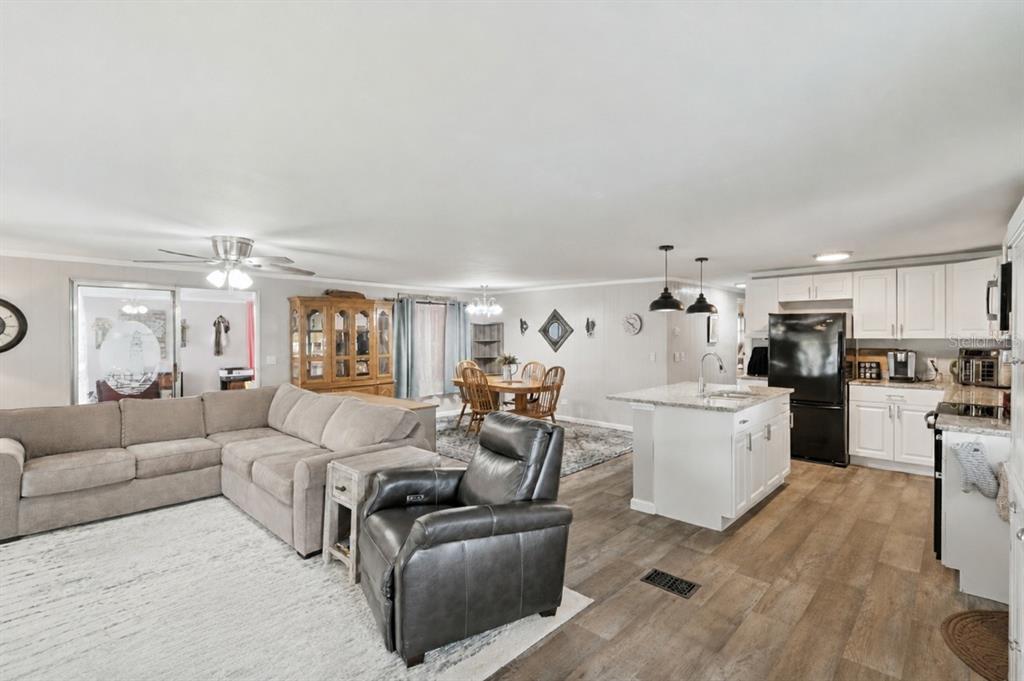 An open-concept living room and kitchen with white cabinets, a kitchen island, and wood flooring — 332 HAWTHORNE BOULEVARD, LEESBURG, FL