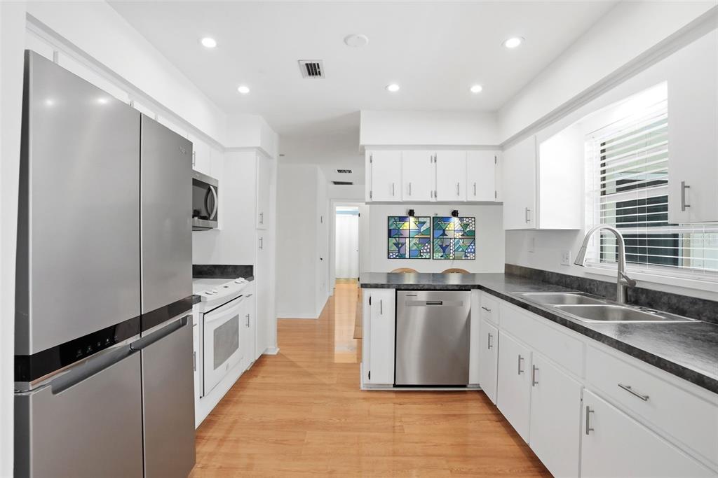 A kitchen with white cabinets, stainless steel appliances, dark countertops, and light wood flooring — 8040 TOWNE COURT, ORLANDO, FL