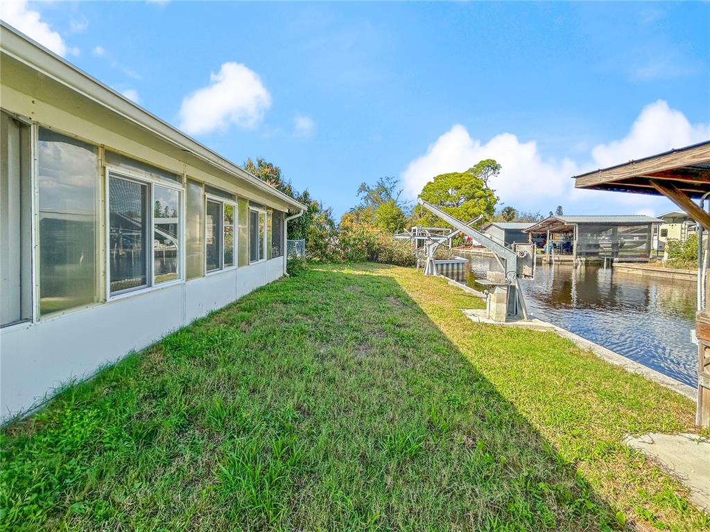 A boat lift with a metal roof sits over a canal next to a grassy bank — 133 NW 18TH STREET, RUSKIN, FL
