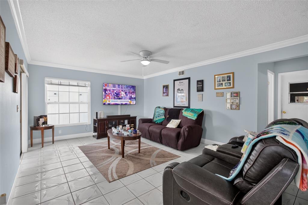 A living room features light blue walls, tile flooring, a ceiling fan, and brown furniture — 1564 LAWNDALE CIRCLE, WINTER PARK, FL