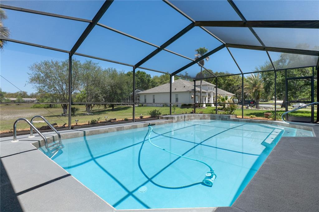 A screened-in swimming pool with a ladder and a blue cleaning hose in a yard — 18652 AUTUMN LAKE BOULEVARD, HUDSON, FL