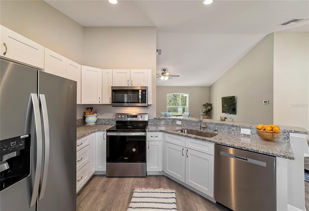 A kitchen with white cabinets, granite countertops, stainless steel appliances, and wood-look flooring — 12997 SW 88TH COURT, OCALA, FL