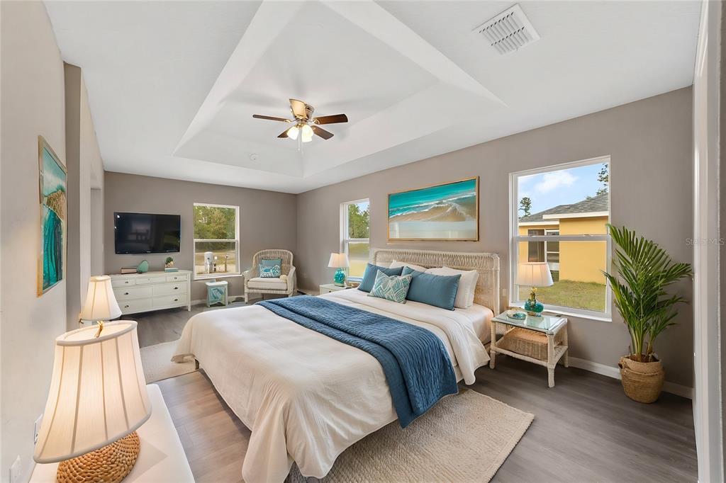 A bedroom with a tray ceiling, light gray walls, wood-look flooring, and a queen-sized bed — 12997 SW 88TH COURT, OCALA, FL