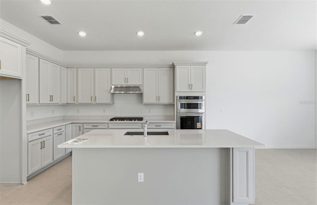 A modern kitchen features light gray cabinets, a large island with a sink, and appliances — 7046 DEPUE DRIVE, WESLEY CHAPEL, FL
