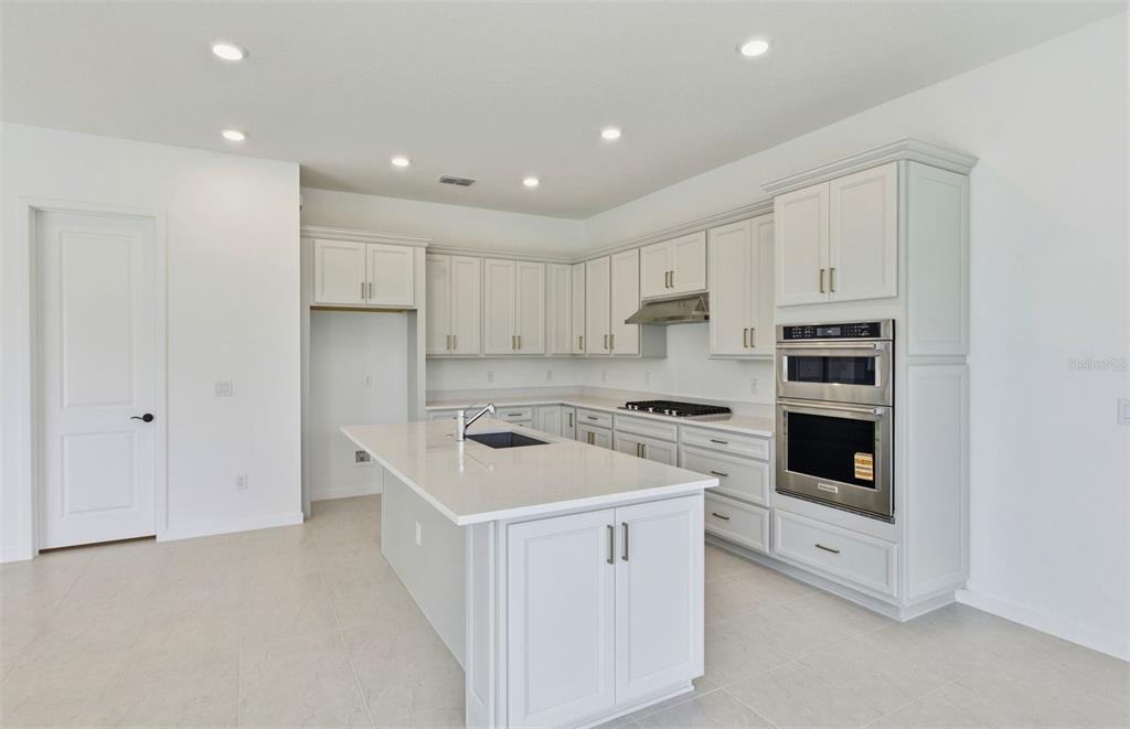 A modern kitchen features light gray cabinets, a central island with a sink, and appliances — 7046 DEPUE DRIVE, WESLEY CHAPEL, FL