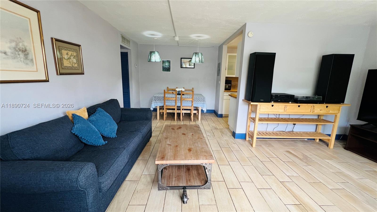 A living room with a dark blue sofa, wooden coffee table, and adjacent dining area — 801 Meridian Ave # 1A, Miami Beach FL 33139, MIAMI BEACH, FL