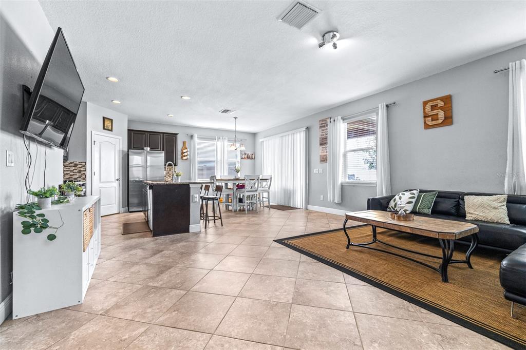 An open-concept living room and kitchen featuring tile flooring, a black sofa, and dining area — 11150 ABACO ISLAND AVENUE, RIVERVIEW, FL