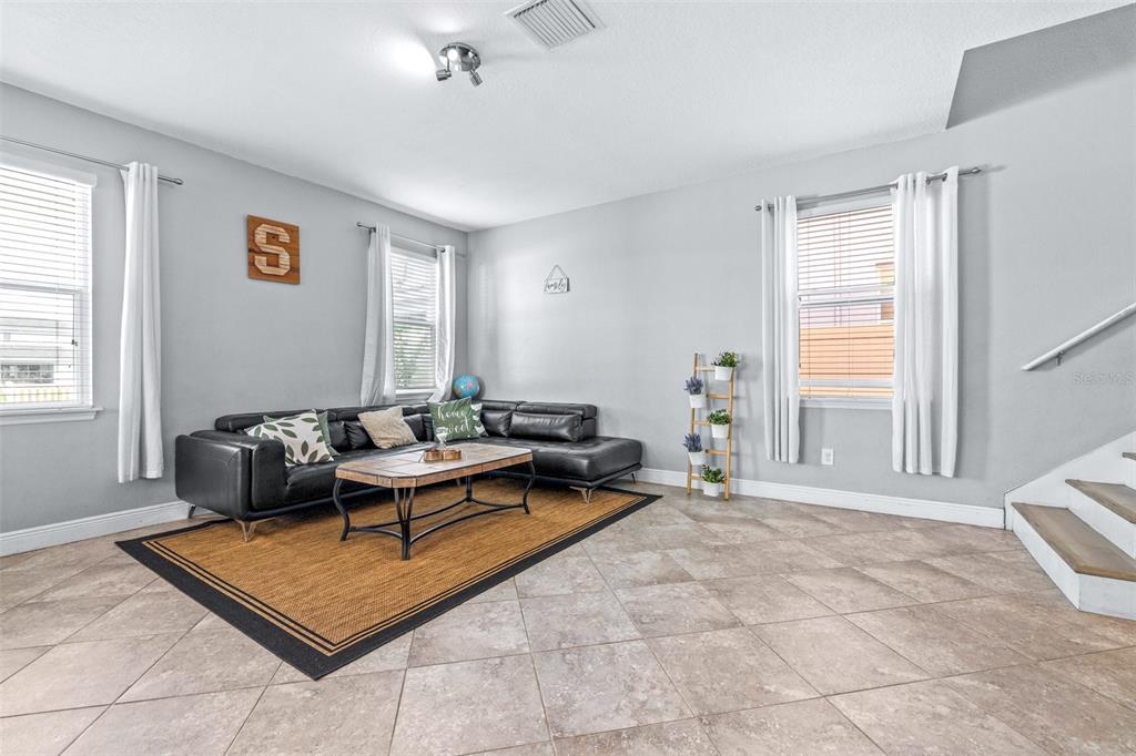 A living room features light gray walls, tile flooring, a black sectional sofa, and stairs — 11150 ABACO ISLAND AVENUE, RIVERVIEW, FL