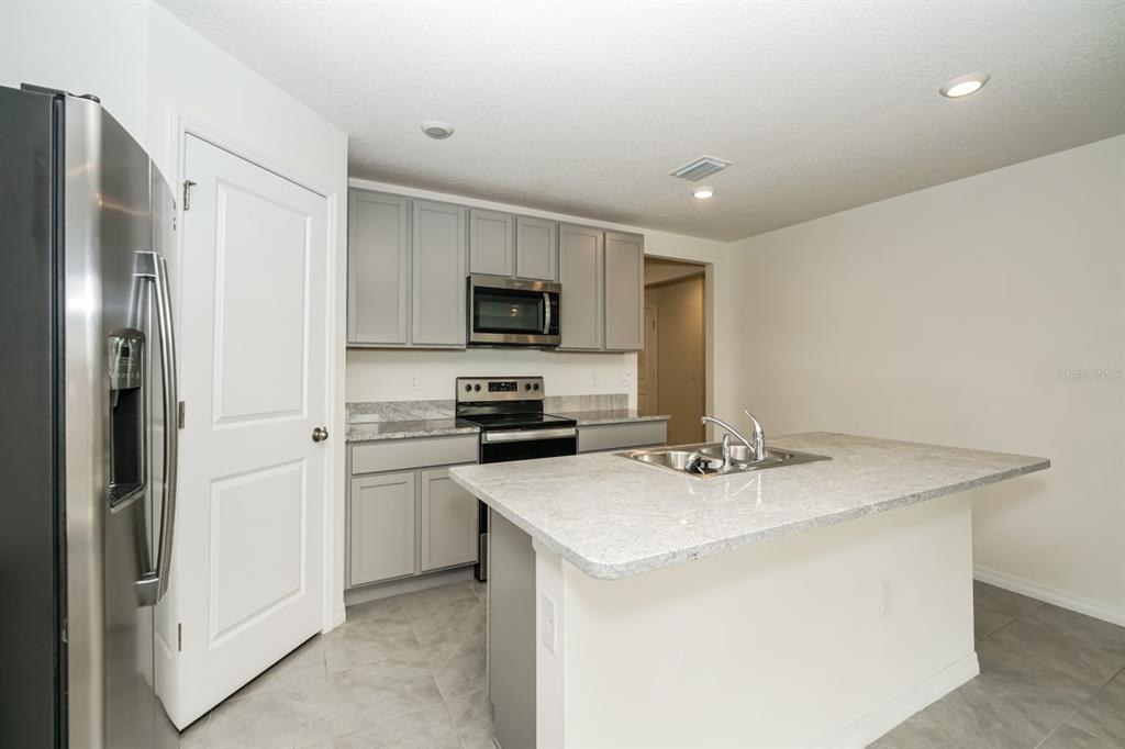 A kitchen features grey cabinets, granite countertops, a stainless steel refrigerator, and a center island — 796 SE 66TH TERRACE, OCALA, FL
