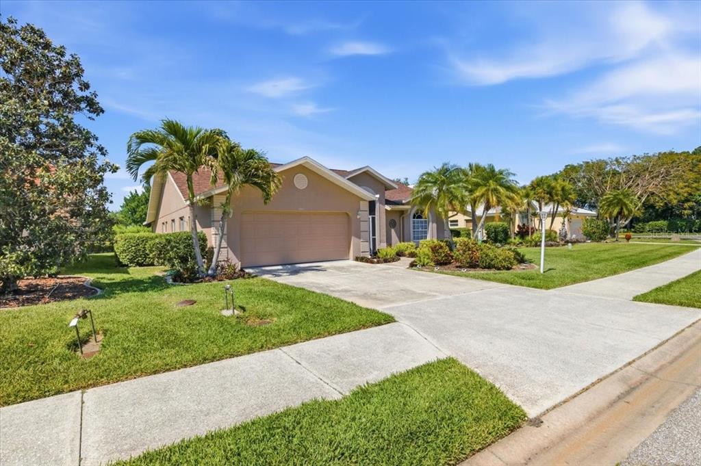 A tan single-story house with a two-car garage and palm trees in the front yard — 7015 PLEASANT HILL ROAD, BRADENTON, FL