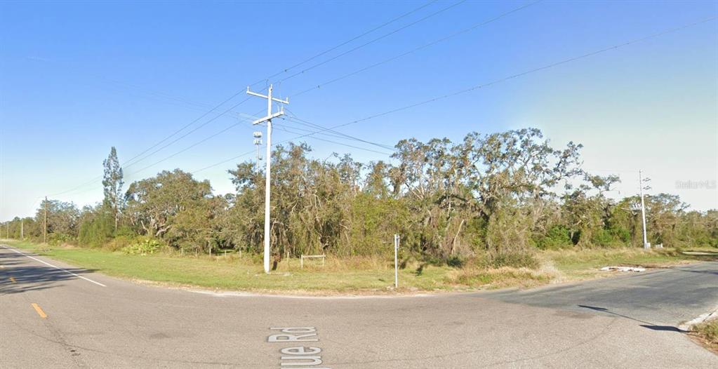 A paved road intersection borders a large, wooded vacant lot with overhead power lines — 37851 STATE ROAD 64 E, MYAKKA CITY, FL