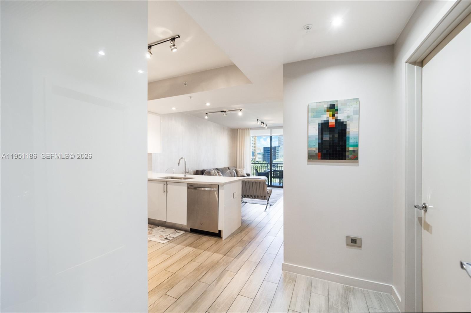 A modern kitchen with white cabinetry and stainless steel appliances opens into a living area — 999 SW 1st Ave # 1208, Miami FL 33130, MIAMI, FL