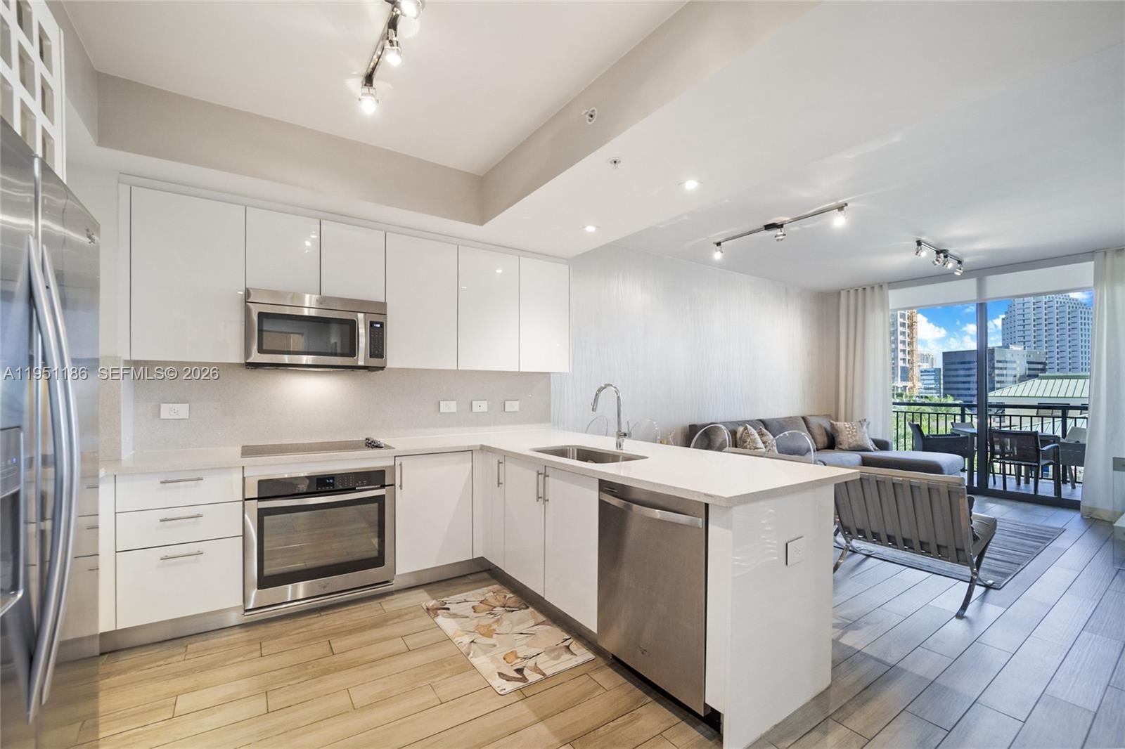 A modern kitchen with white cabinetry and stainless steel appliances opens to a living area — 999 SW 1st Ave # 1208, Miami FL 33130, MIAMI, FL