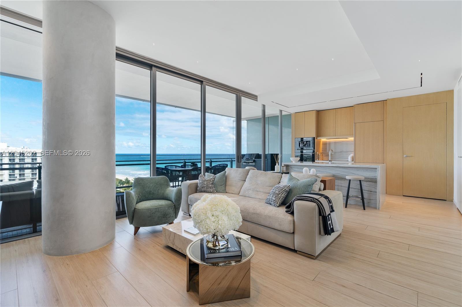 A modern living room features a beige sofa, green armchair, and ocean views through glass walls — 8701 Collins Ave # 1103, Miami Beach FL 33154, MIAMI BEACH, FL