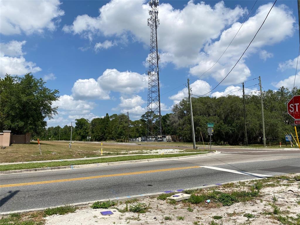 A tall communication tower stands behind a vacant grassy lot near a paved intersection — 8357 BELLA CITTA BOULEVARD, DAVENPORT, FL