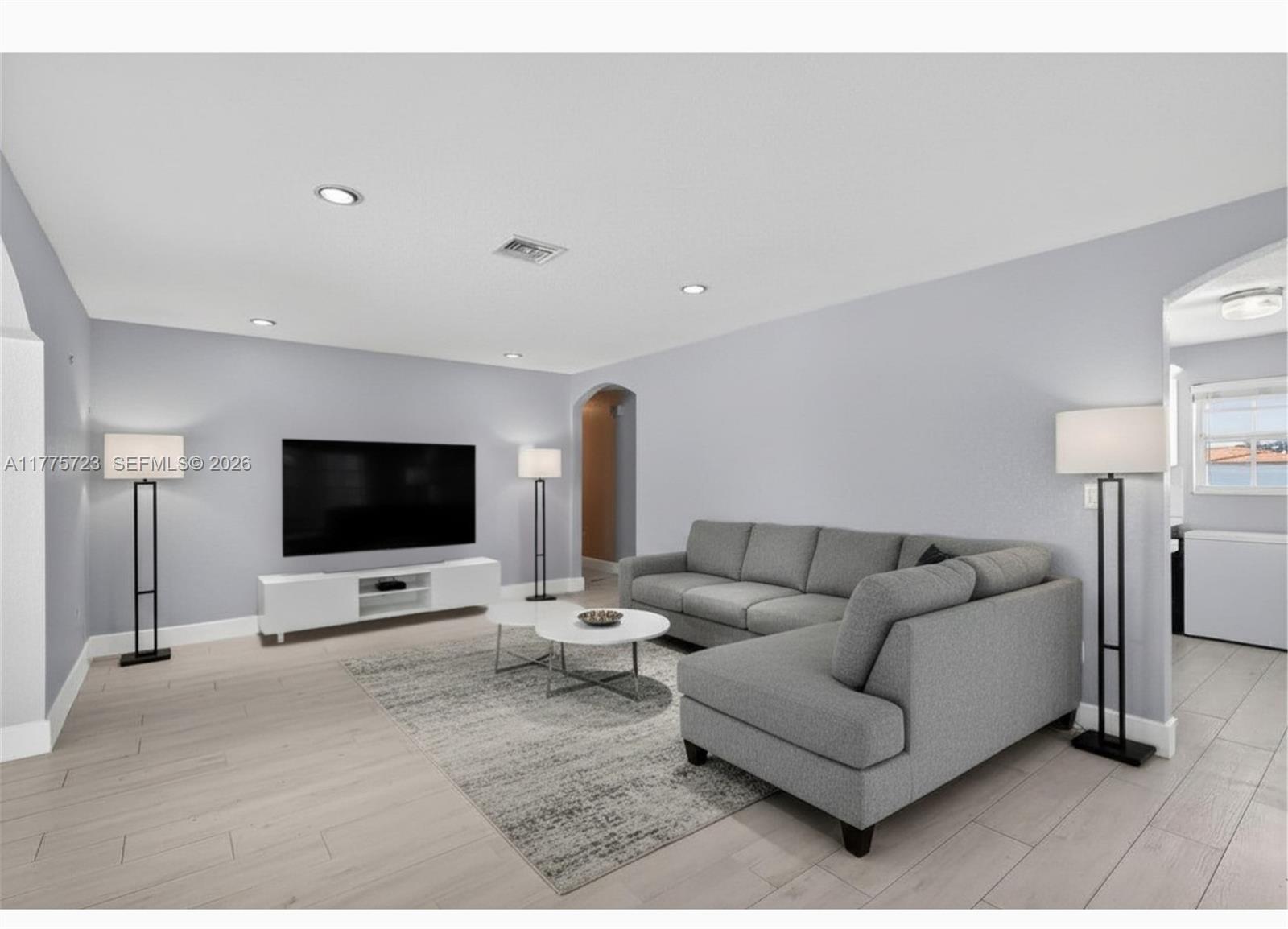 A living room features a gray sectional sofa, a wall-mounted television, and light wood flooring — 217 SE 5th St, Dania Beach FL 33004, DANIA BEACH, FL