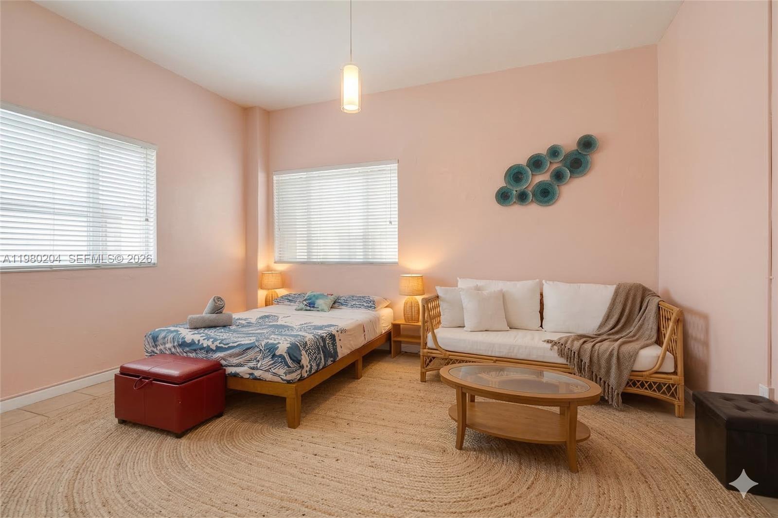 A bedroom features a bed, a rattan sofa, and a coffee table on a rug — 255 W 24th St # 107, Miami Beach FL 33140, MIAMI BEACH, FL