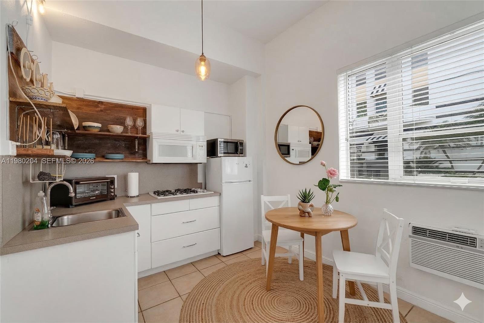 A small kitchen features white cabinets, open wood shelving, and a round dining table — 255 W 24th St # 107, Miami Beach FL 33140, MIAMI BEACH, FL