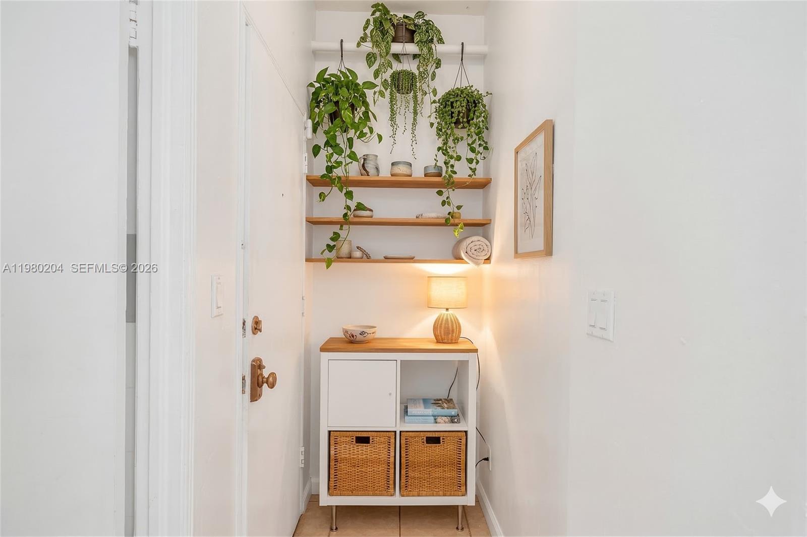A small entryway nook features a white storage cabinet, floating shelves, and hanging plants — 255 W 24th St # 107, Miami Beach FL 33140, MIAMI BEACH, FL