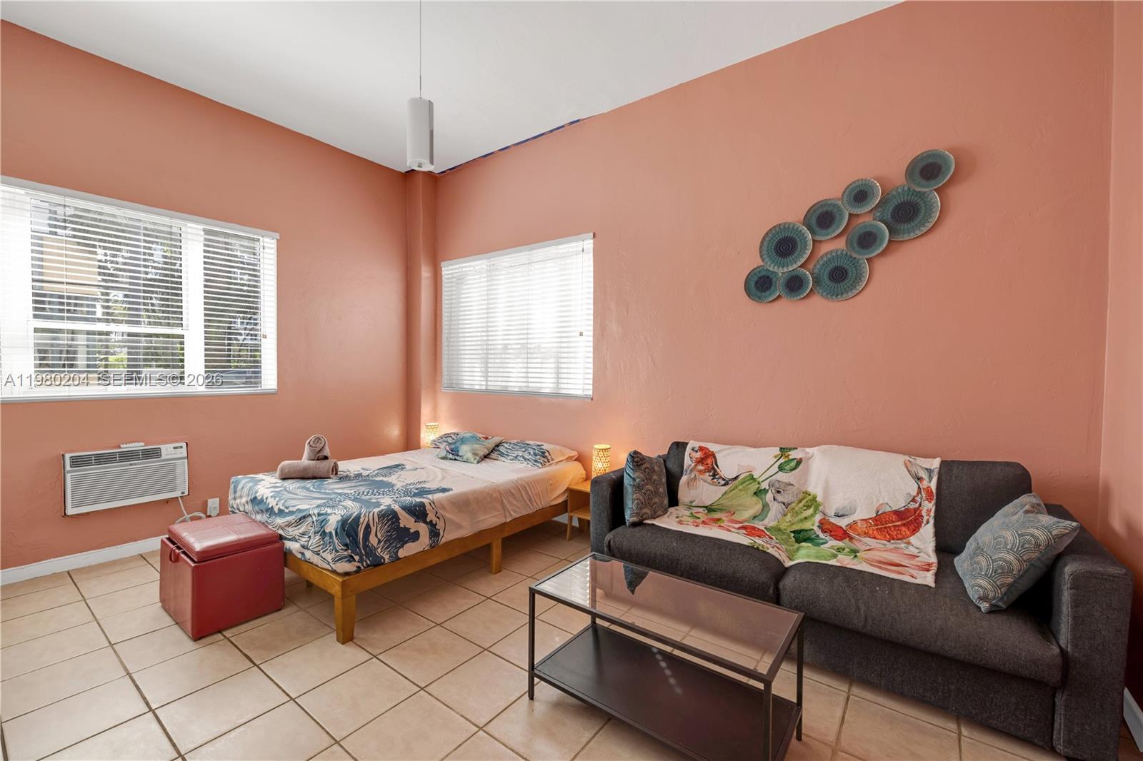 A bedroom features peach-colored walls, tile flooring, a bed, and a dark gray sofa — 255 W 24th St # 107, Miami Beach FL 33140, MIAMI BEACH, FL