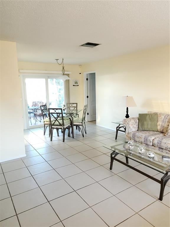 A living and dining area with light-colored tile floors, a glass-top table, and sliding doors — 6316 16TH AVENUE DRIVE W, BRADENTON, FL