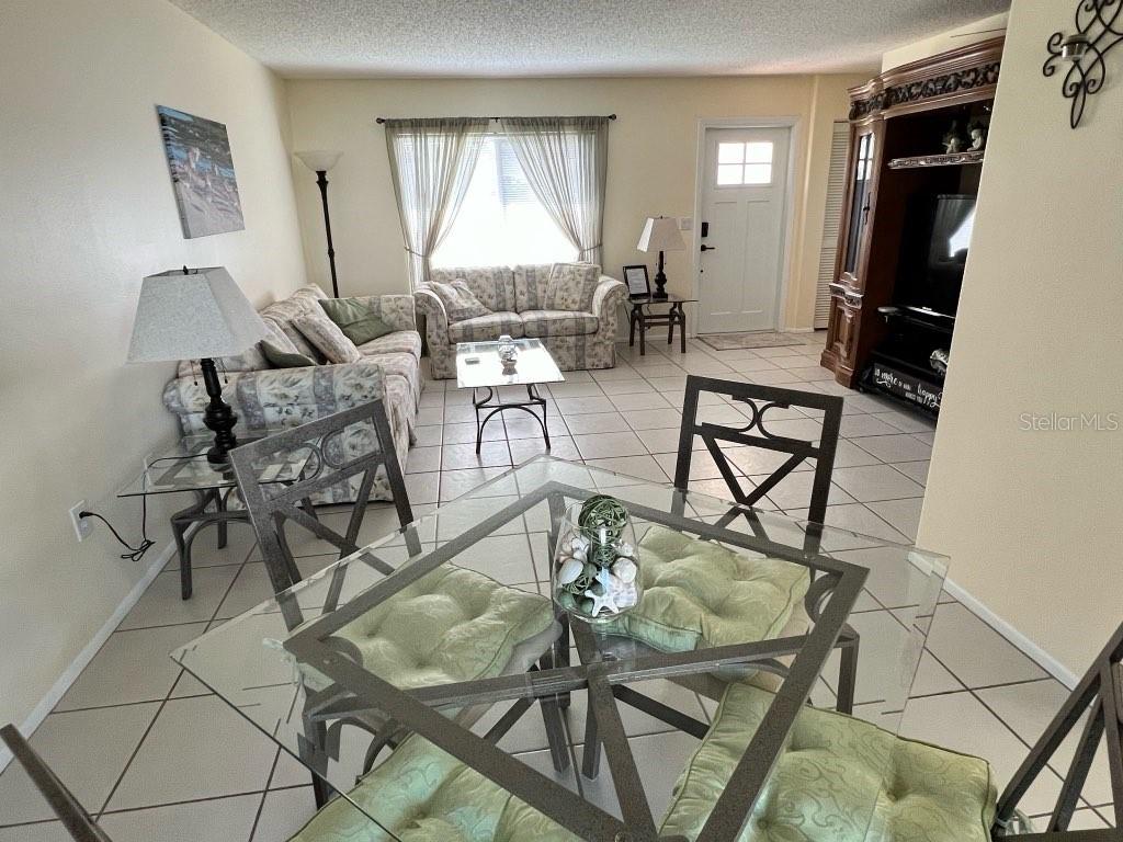A living room and dining area featuring tile flooring, floral furniture, and a glass table — 6316 16TH AVENUE DRIVE W, BRADENTON, FL