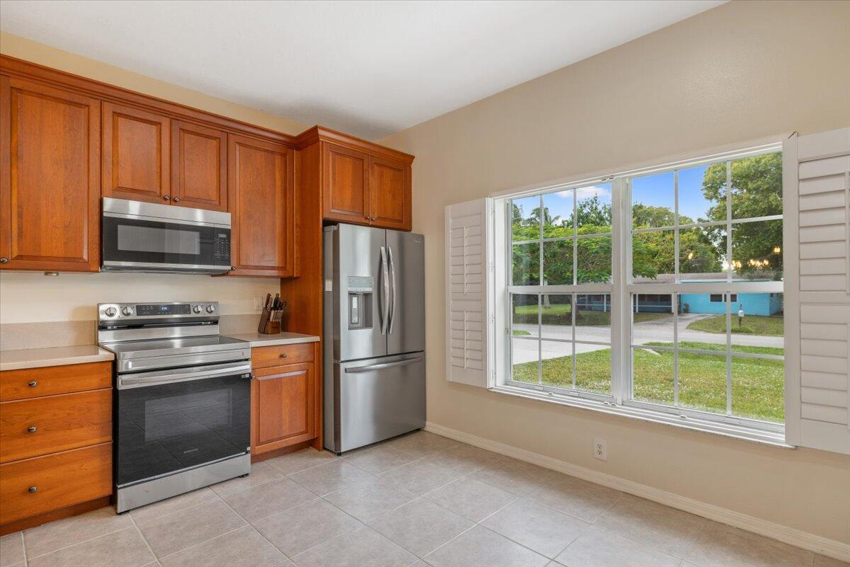 A kitchen features wood cabinets, stainless steel appliances, tile flooring, and a large window — 1410 4th Court, Vero Beach FL 32960, VERO BEACH, FL