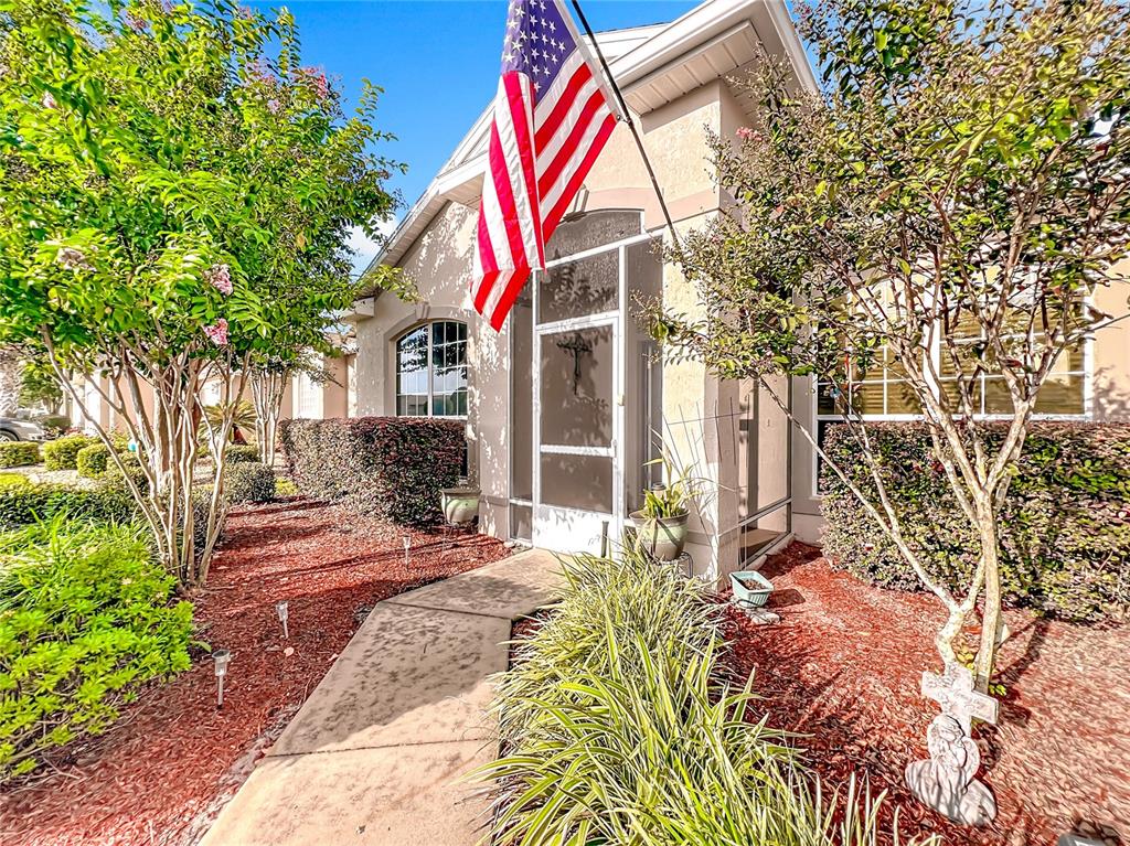 A concrete walkway leads to a screened front entryway with an American flag displayed above — 1732 SW 157TH PLACE ROAD, OCALA, FL