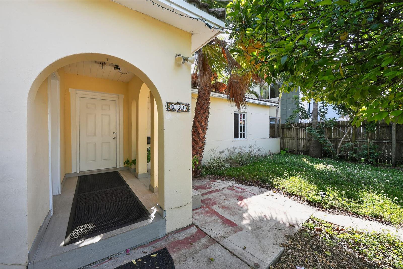 A yellow house exterior features an arched entryway, a concrete patio, and a palm tree — 2131 Biarritz Drive, Miami Beach FL 33141, MIAMI BEACH, FL