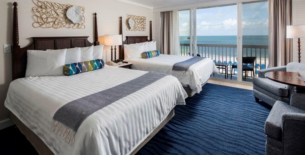 A hotel room features two beds, a blue patterned rug, and a balcony overlooking the ocean — 5500 GULF BOULEVARD UNIT 3219, ST PETE BEACH, FL
