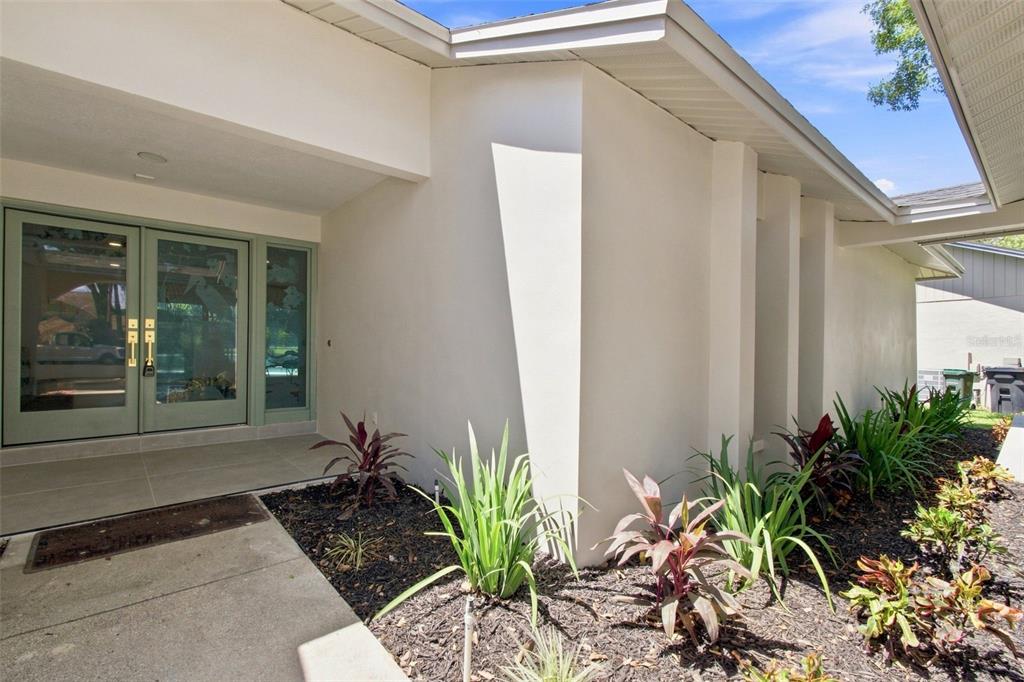 A modern home entrance features double glass doors, a concrete porch, and landscaped garden beds — 3126 EDGEMOOR DRIVE, PALM HARBOR, FL