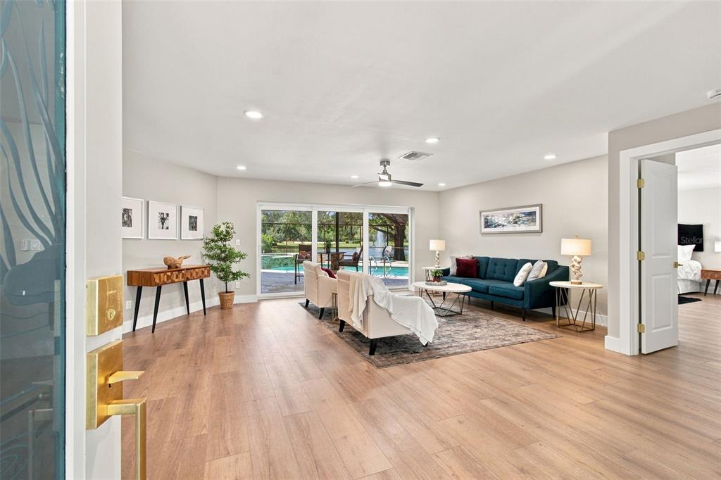 A living room features light wood floors, a blue sofa, and sliding doors to a pool — 3126 EDGEMOOR DRIVE, PALM HARBOR, FL