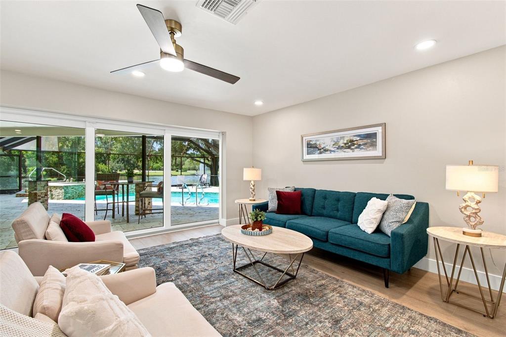 A living room features a teal sofa, light-colored armchairs, and sliding glass doors overlooking a pool — 3126 EDGEMOOR DRIVE, PALM HARBOR, FL