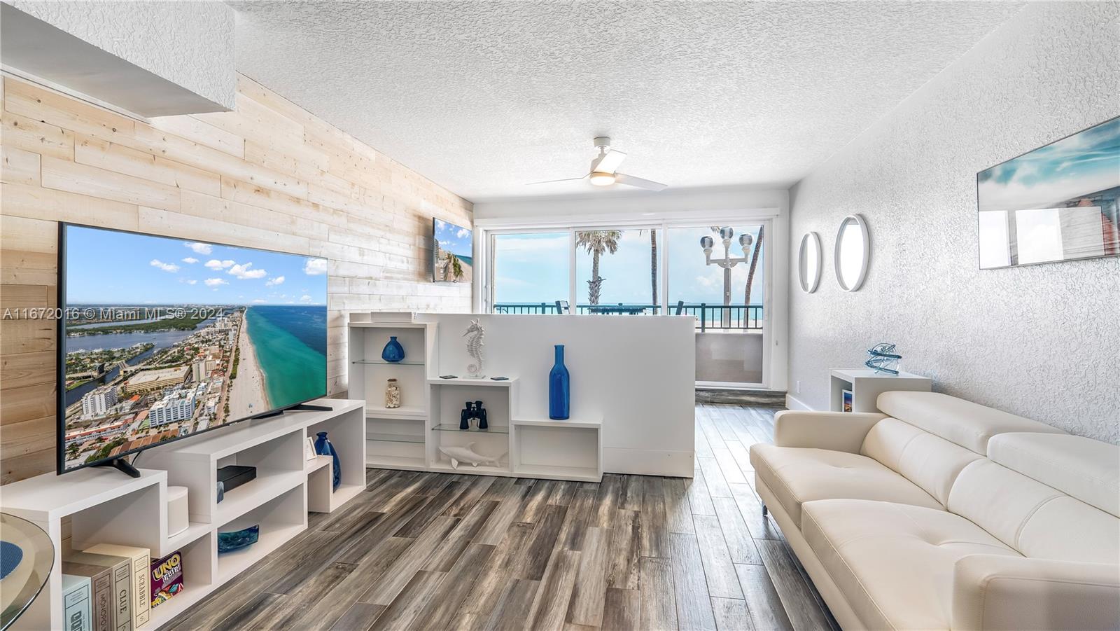 A living room features a wood-paneled accent wall, white shelving, and a view of the ocean — 201 Van Buren St # 103, Hollywood FL 33019, HOLLYWOOD, FL