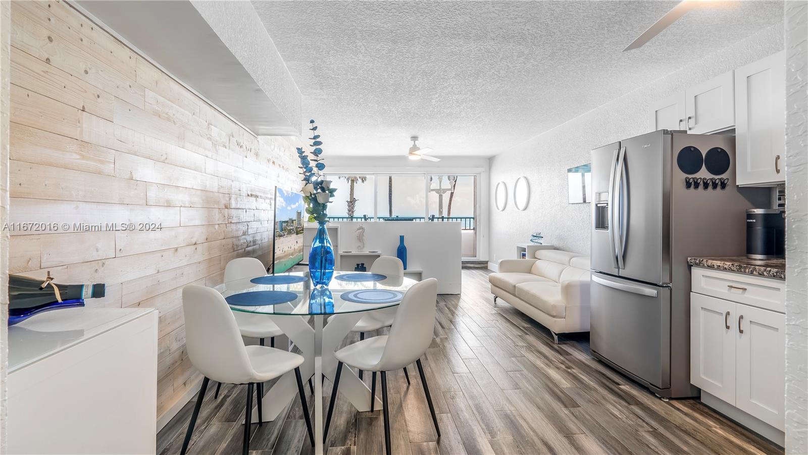 A bright open-concept living and dining area features wood-look flooring, white furniture, and a kitchen — 201 Van Buren St # 103, Hollywood FL 33019, HOLLYWOOD, FL