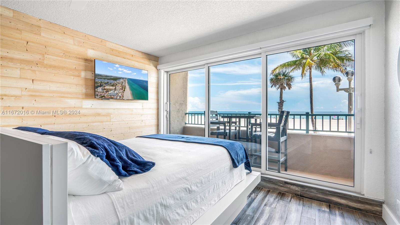 A bedroom features a wood-paneled wall, a platform bed, and sliding glass doors overlooking the ocean — 201 Van Buren St # 103, Hollywood FL 33019, HOLLYWOOD, FL