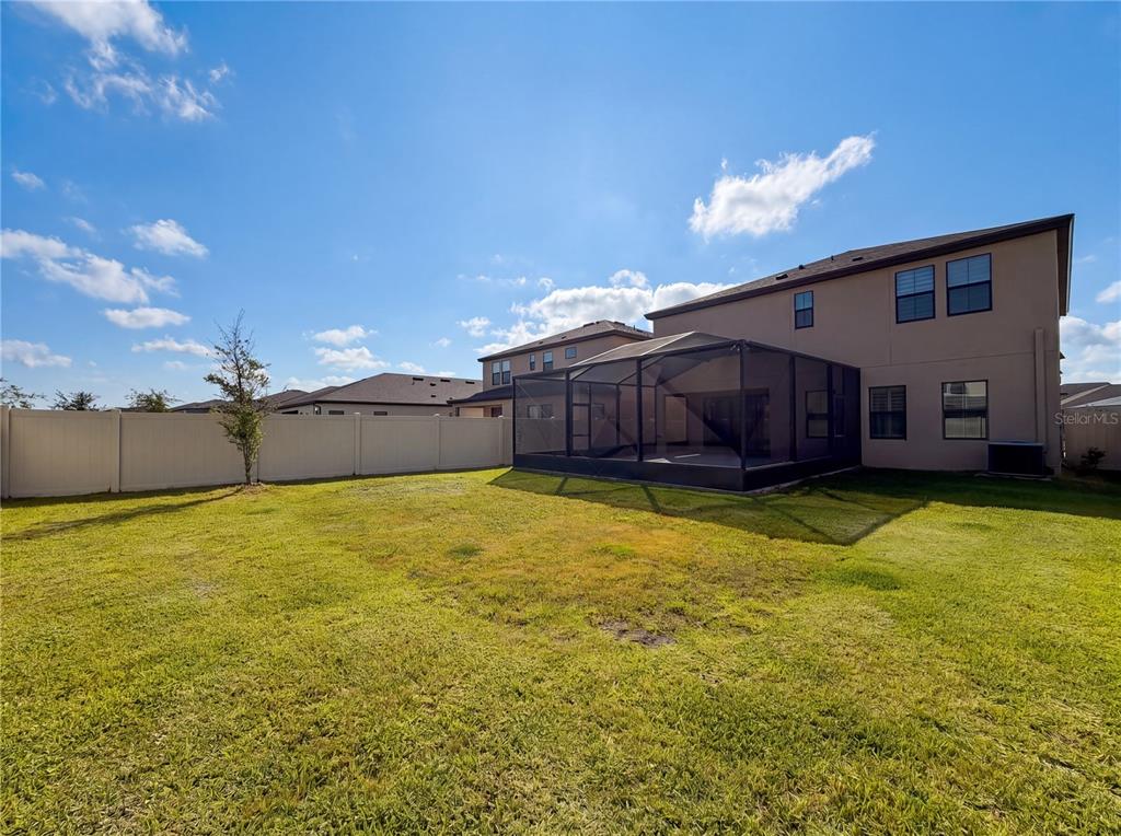 A backyard with a grass lawn, a white vinyl fence, and a screened-in patio — 12643 HORSESHOE BEND DRIVE, LITHIA, FL