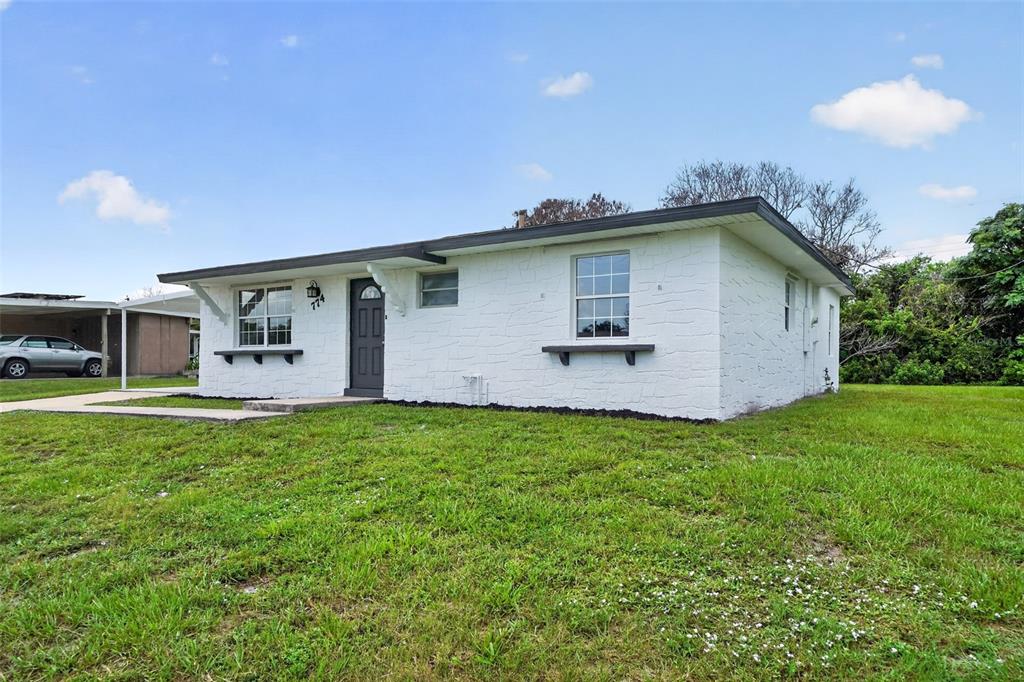 A white, single-story house with a dark front door and a grassy front yard — 774 HAMPTON DRIVE NE, PALM BAY, FL