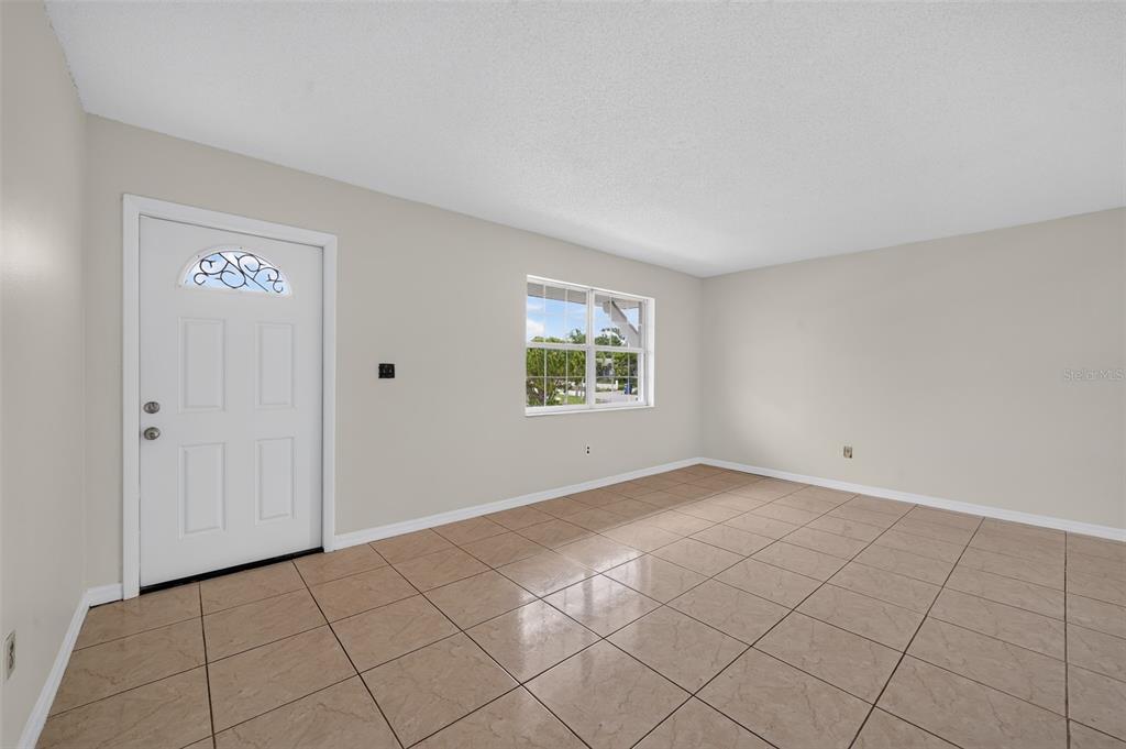 An empty room features beige tile flooring, light-colored walls, a white front door, and windows — 774 HAMPTON DRIVE NE, PALM BAY, FL