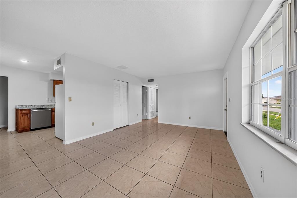 An open-concept living area with light-colored tile flooring, white walls, and an adjacent kitchen — 774 HAMPTON DRIVE NE, PALM BAY, FL