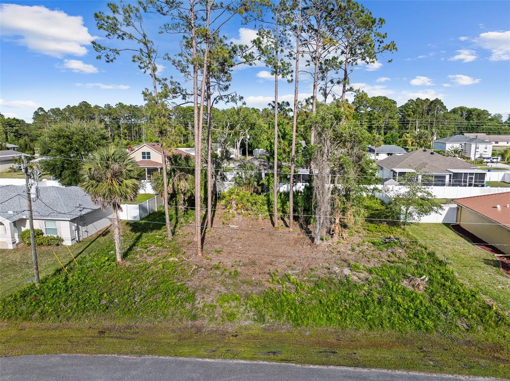 An elevated view of a vacant, tree-covered residential lot situated between two existing houses — 7 ZEALAND PLACE, PALM COAST, FL